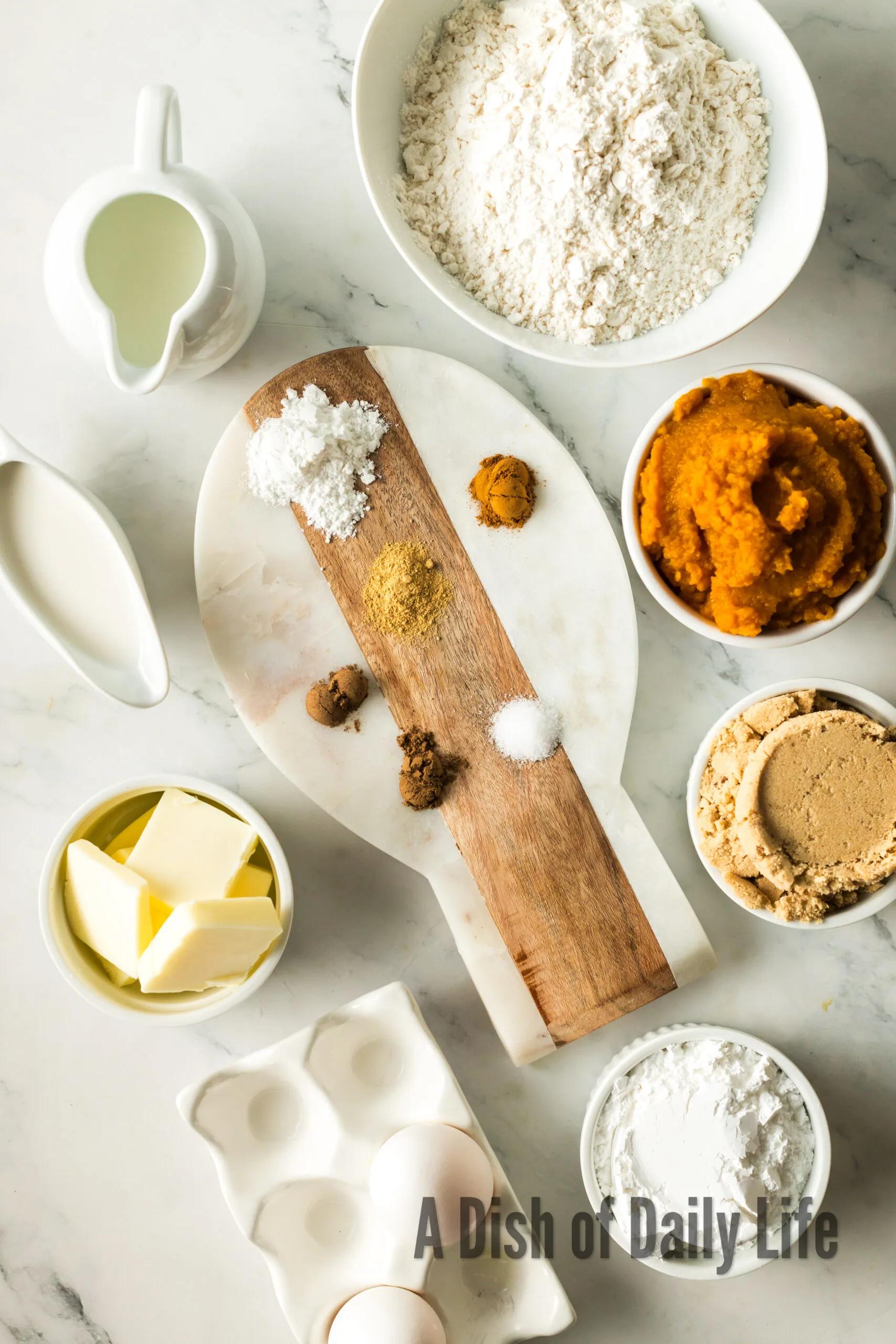 ingredients for pumpkin cinnamon muffins laid out on a kitchen counter, including pumpkin puree, spices, and flour