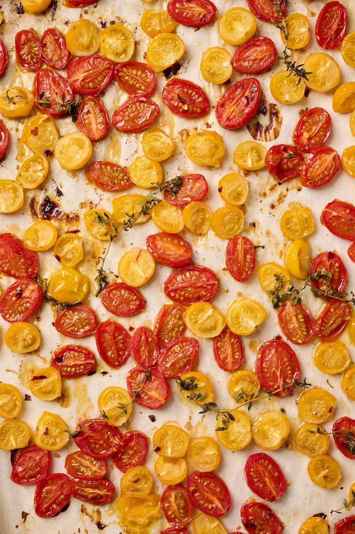 vibrant close-up of cherry tomatoes roasting on a sheet pan with olive oil and herbs, slightly caramelized