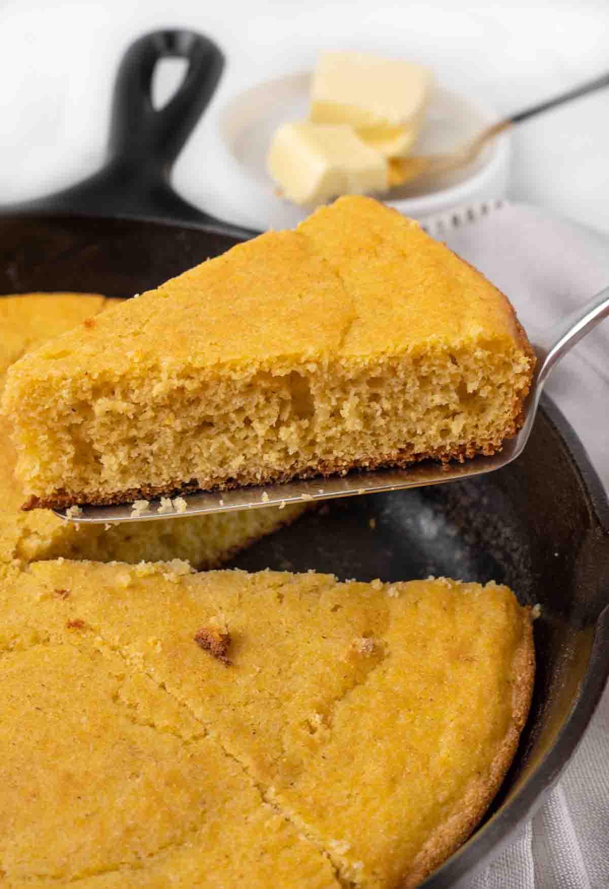 slice of cornbread being removed from a cast iron skillet