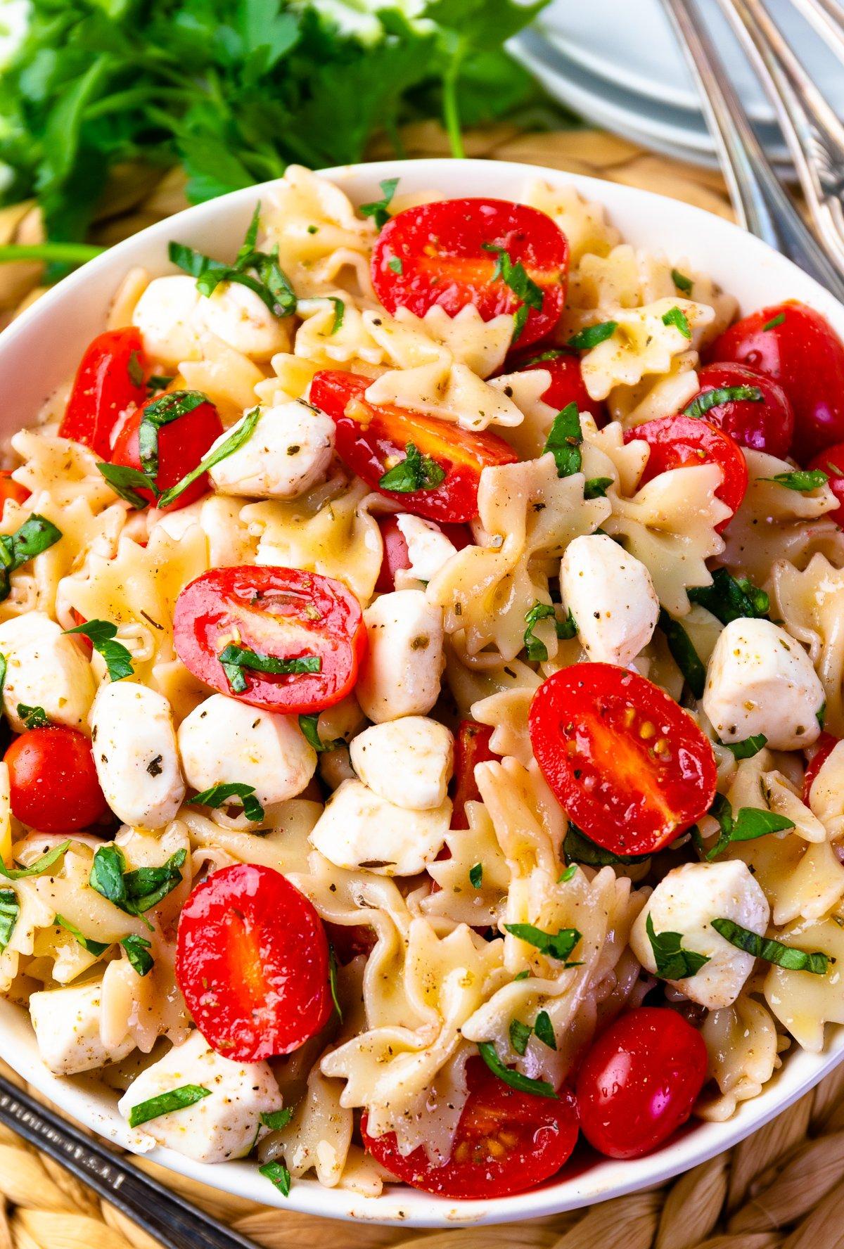 Ingredients for Caprese pasta salad, including mozzarella balls, cherry tomatoes, basil, and sun-dried tomatoes