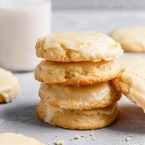 A stack of golden-brown orange zest cookies on a white plate, with a scattering of orange peels.