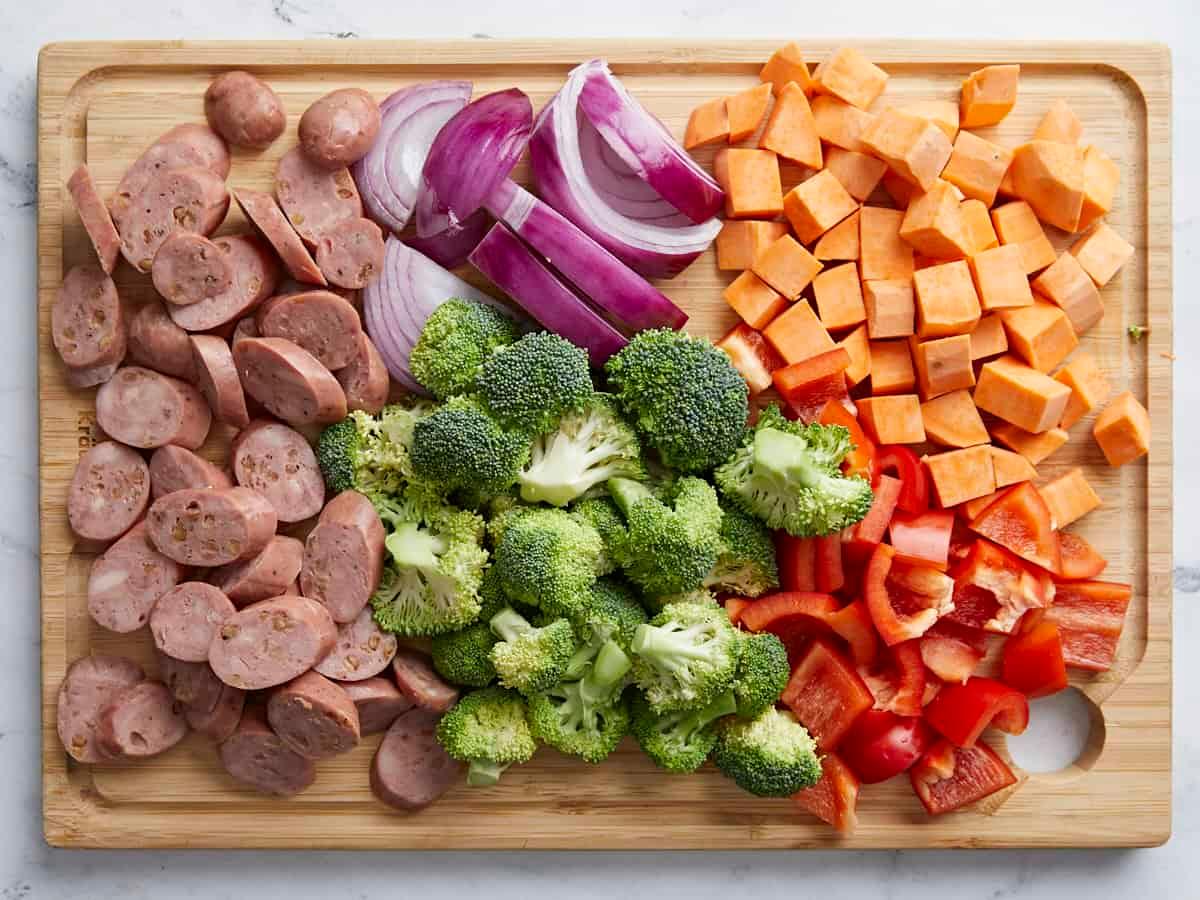 various fresh vegetables and cooked sausage being chopped on a cutting board next to a mixing bowl with eggs