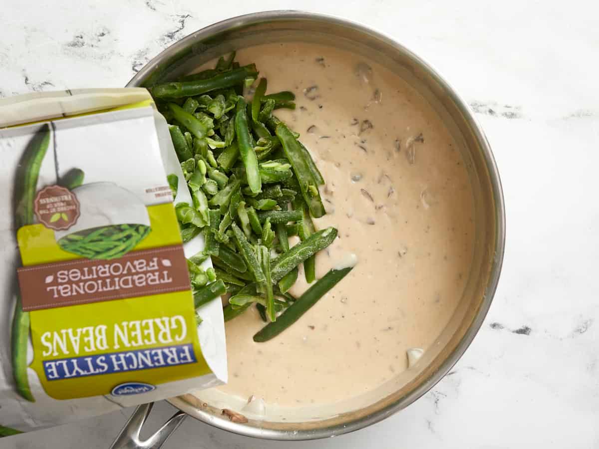 Hands mixing green beans with creamy soup in a glass baking dish