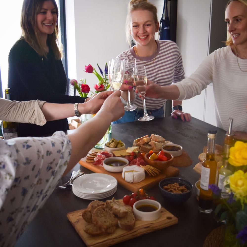 Host casually arranging a charcuterie board with friends chatting in the background, relaxed atmosphere