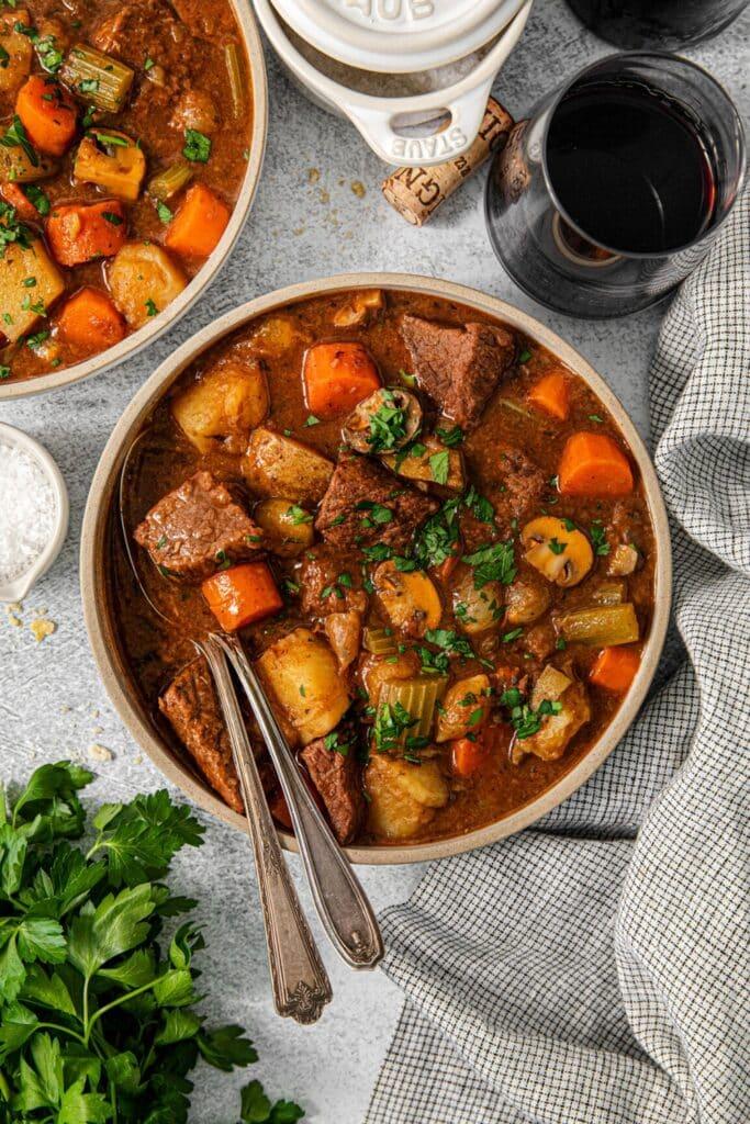 A rustic table setting with a large pot of beef stew, individual bowls, and fresh herbs