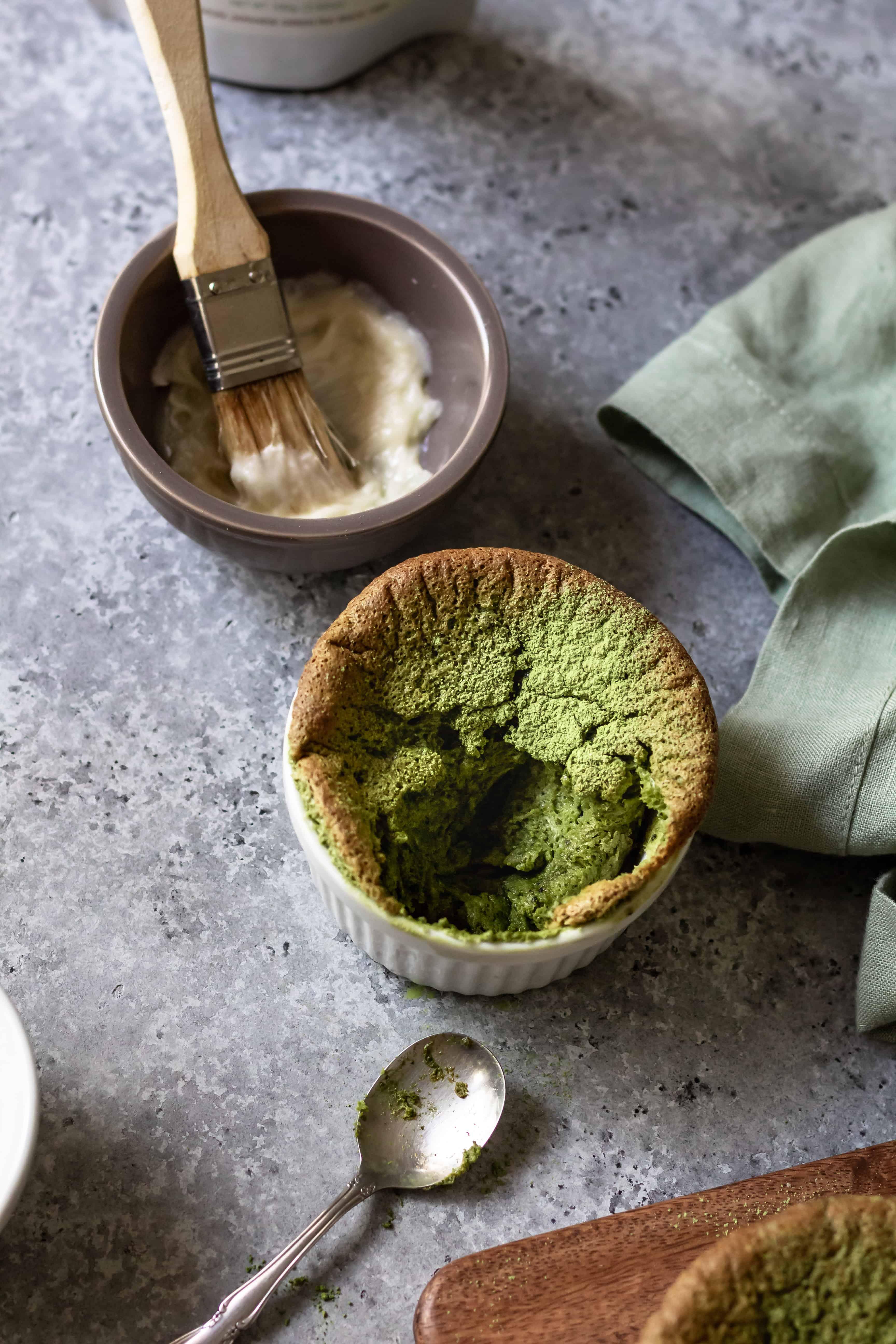 A matcha souffle broken open with a spoon, revealing a soft, molten center.