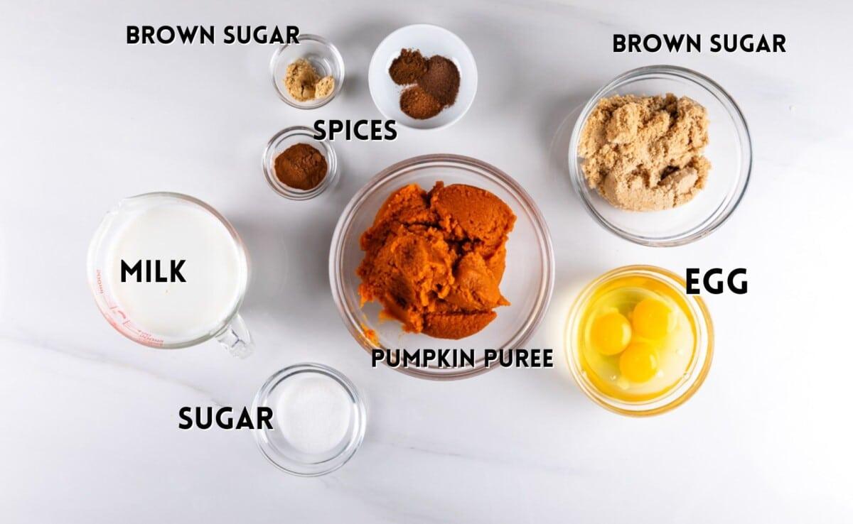 Ingredients for pumpkin pie laid out on a wooden counter, including pumpkin puree can, spices, and eggs