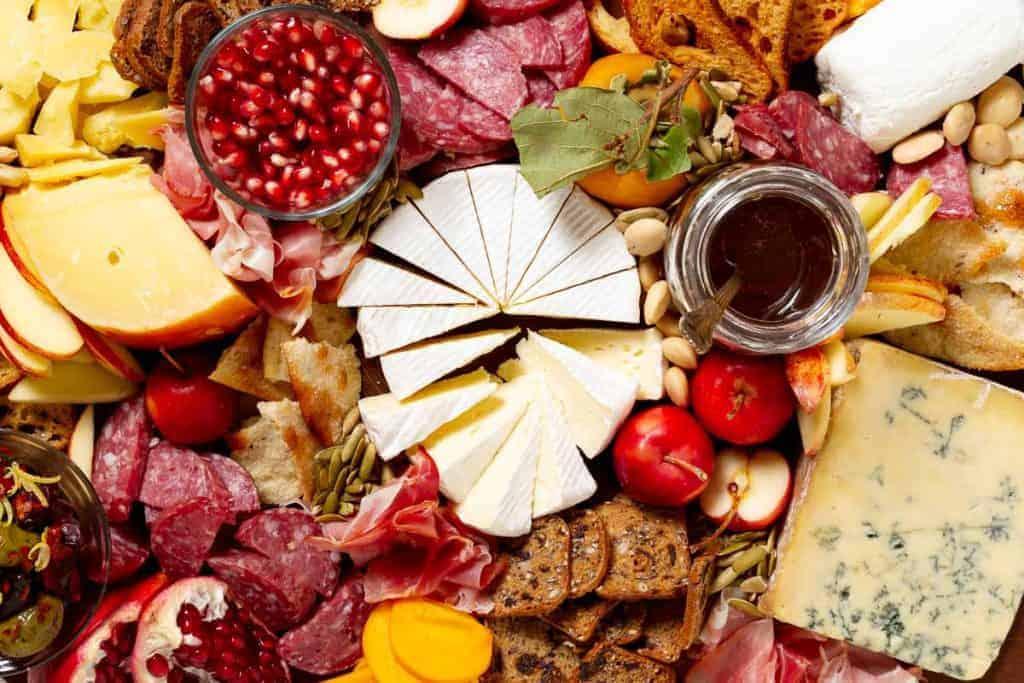 Close-up of a hand selecting a piece of cheese from the cranberry and walnut charcuterie board