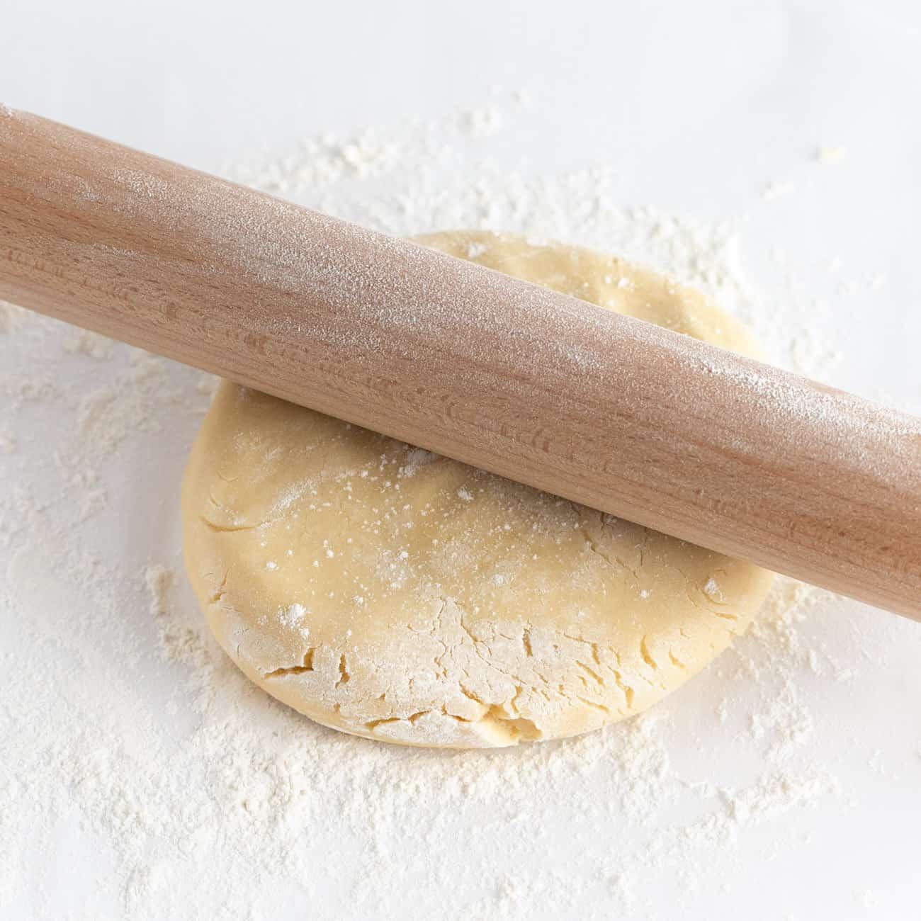 Soft sugar cookie dough being gently rolled out on a floured surface