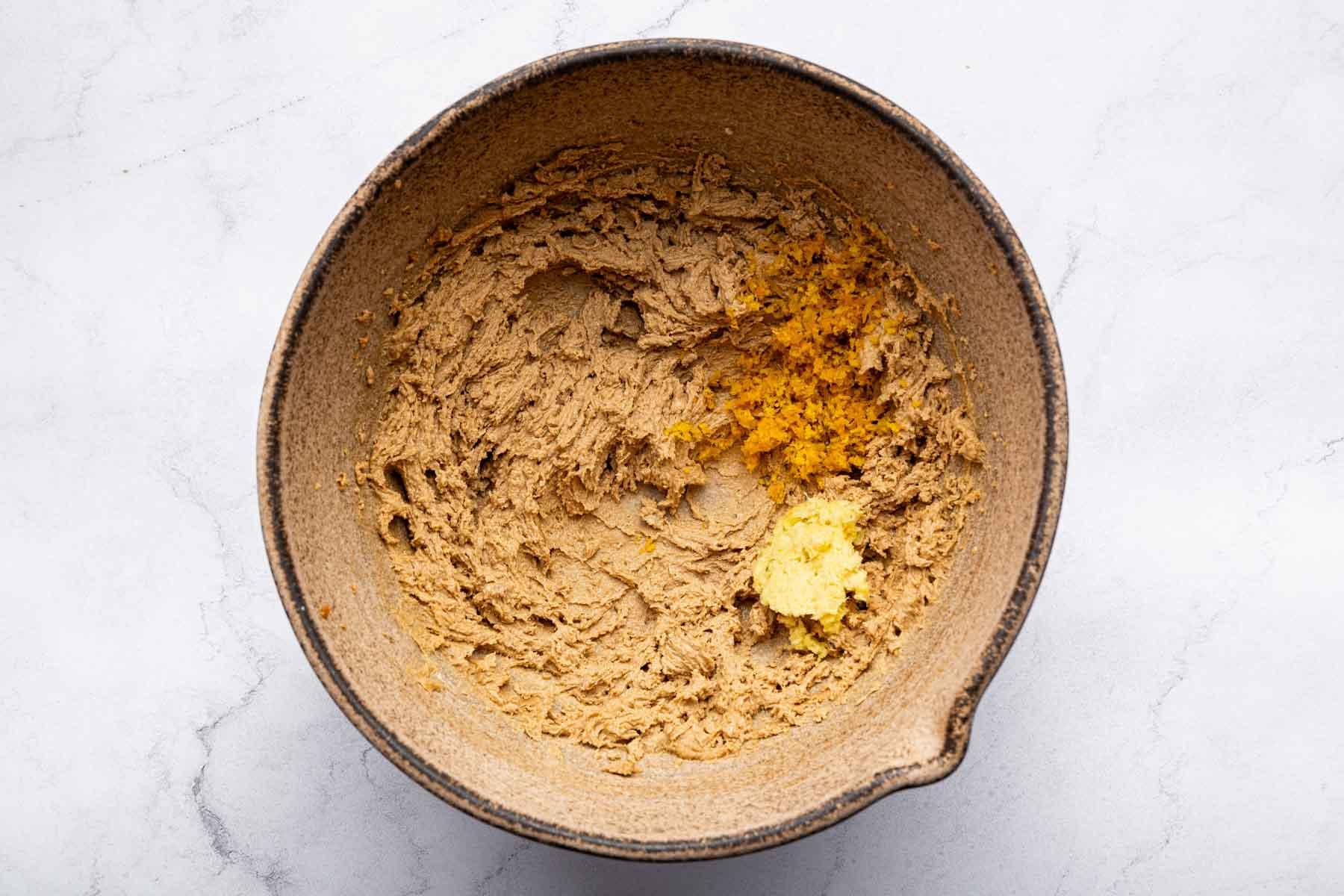 Close-up of fresh orange zest being grated over a bowl of gingerbread cookie dough