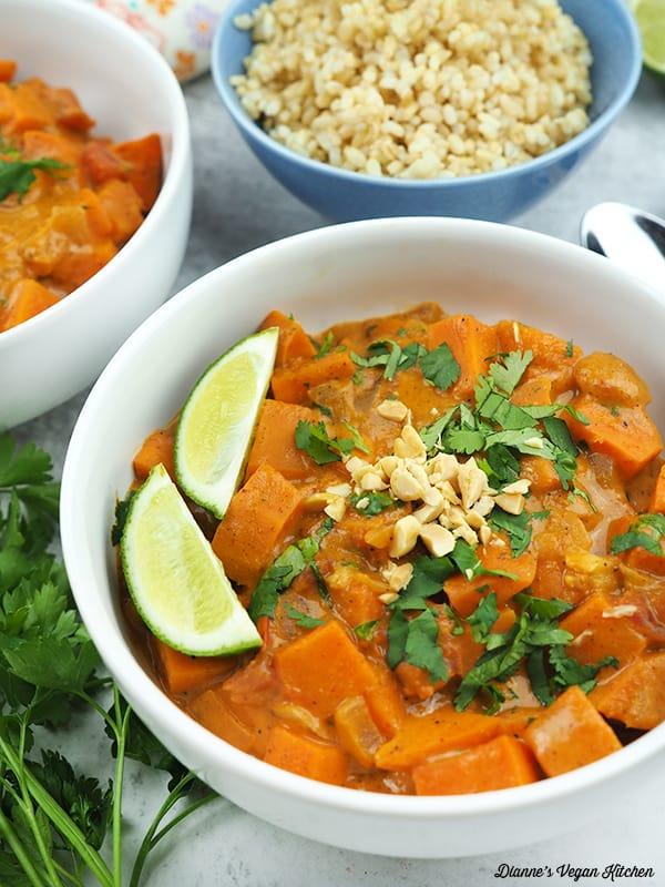close-up of vibrant sweet potato coconut curry in a rustic ceramic bowl with a spoon, garnished with fresh cilantro and a lime wedge