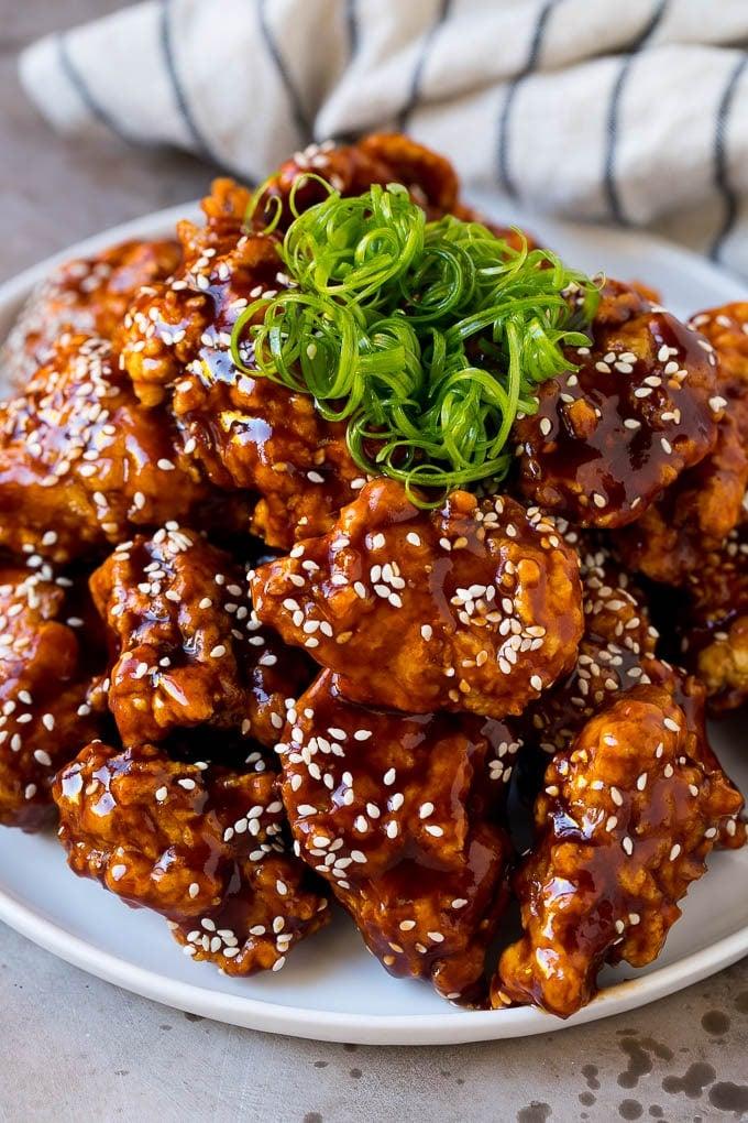 Crispy sweet and spicy chicken thighs with glaze on a plate, garnished with sesame seeds and green onions