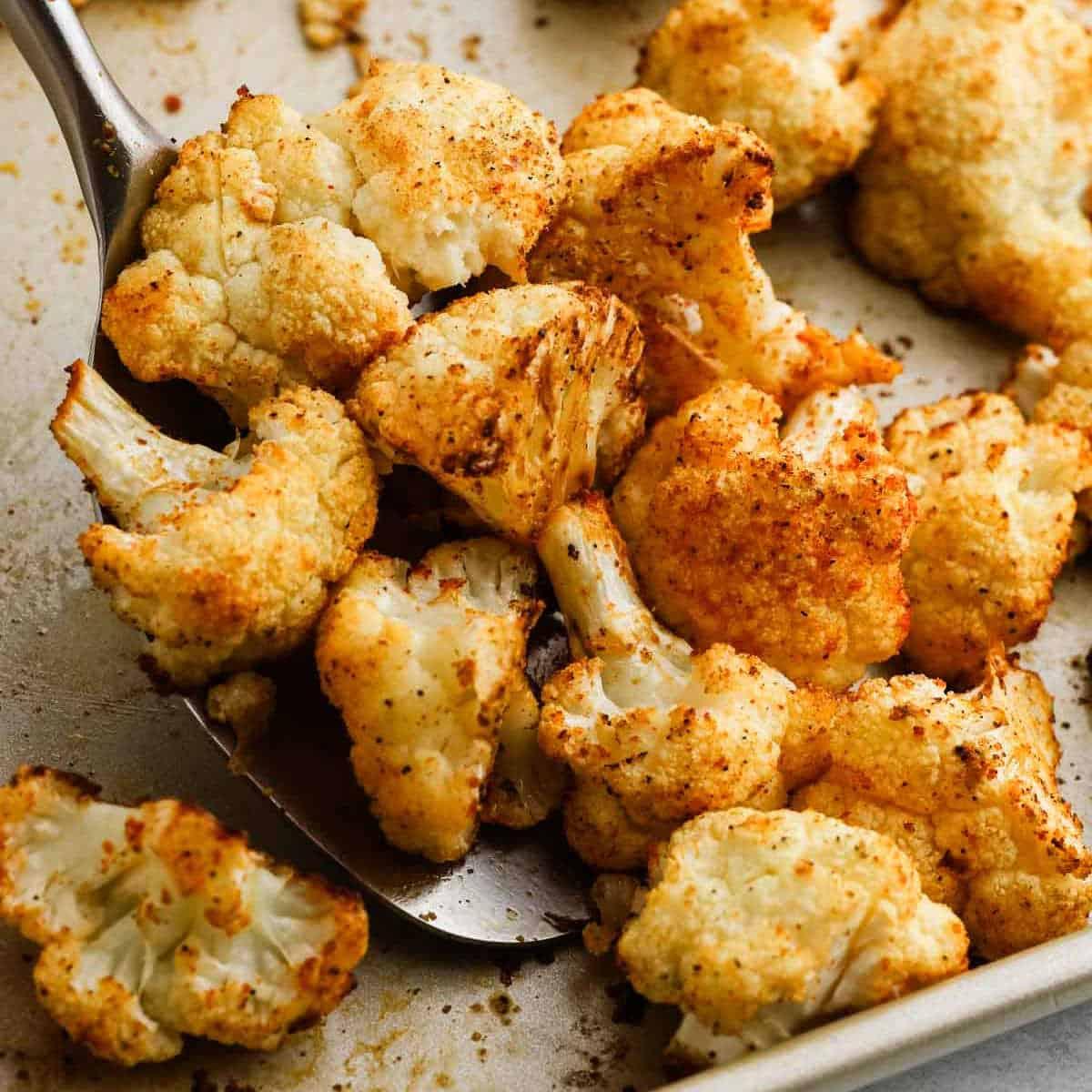 Crispy golden garlic roasted cauliflower florets on a baking sheet, close up