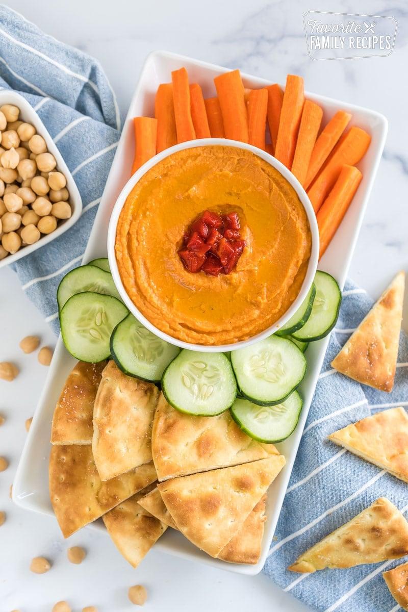 freshly made roasted red pepper hummus served with warm pita bread and colorful vegetable sticks on a wooden board