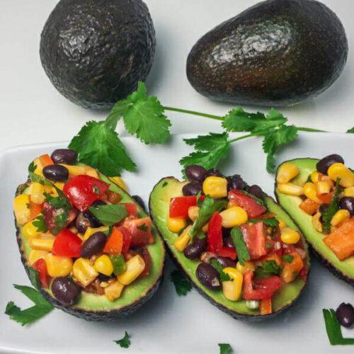 Overhead shot of several black bean and corn stuffed avocados arranged on a plate, garnished with cilantro and lime wedges