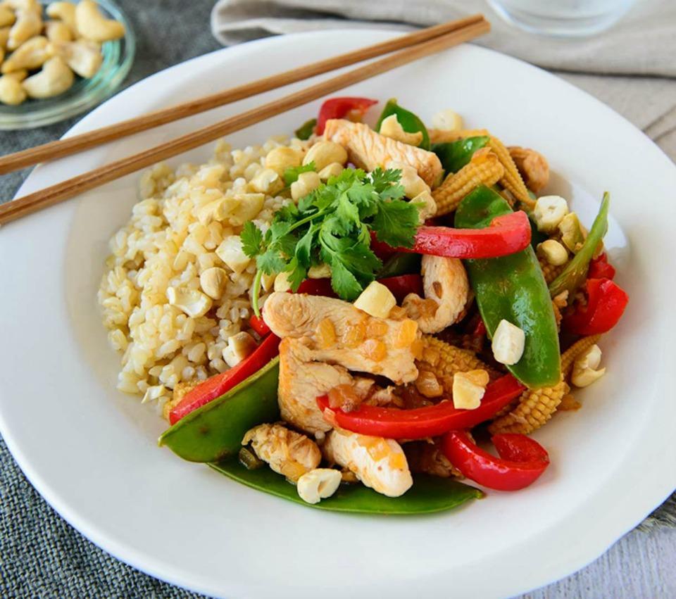 a pregnant woman smiling while eating chicken stir-fry with brown rice