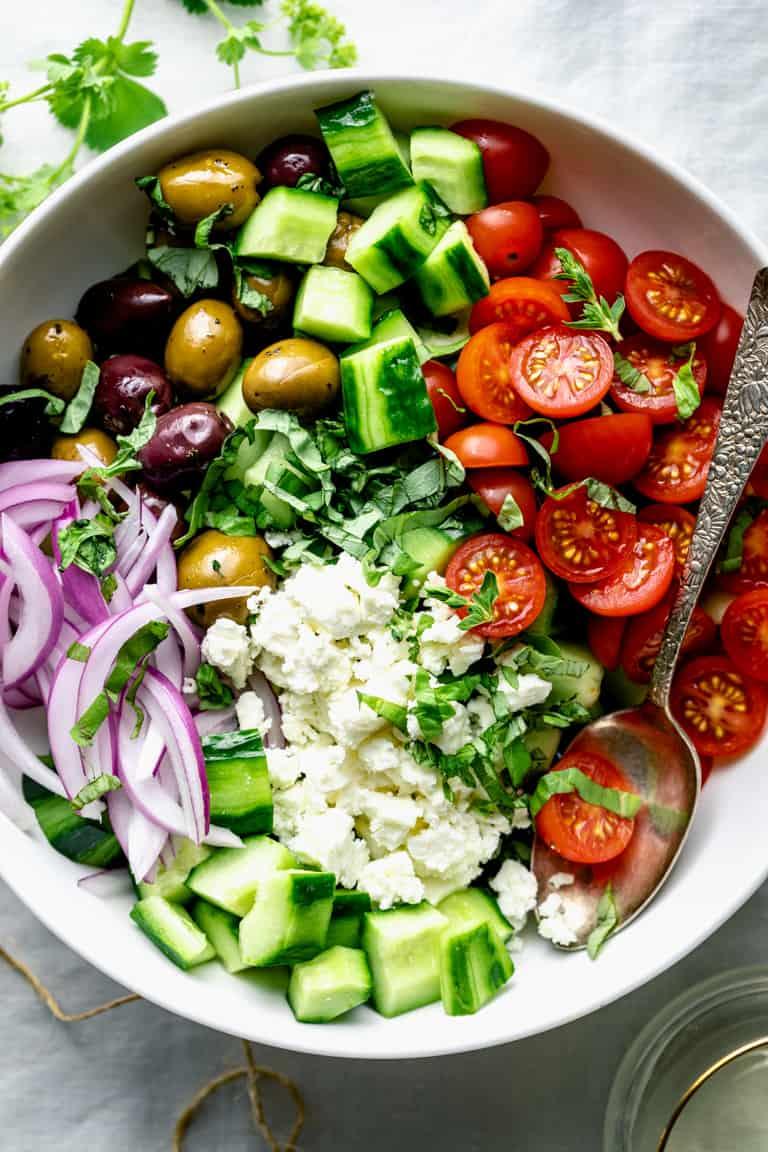 Chopped fresh vegetables including cucumber, cherry tomatoes, red onion, and Kalamata olives in a bowl, ready for a Greek salad