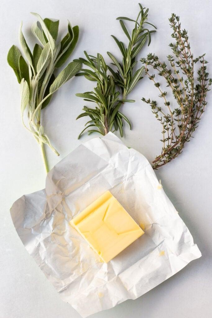 fresh herbs like rosemary, thyme, and sage bundled together, next to a stick of butter