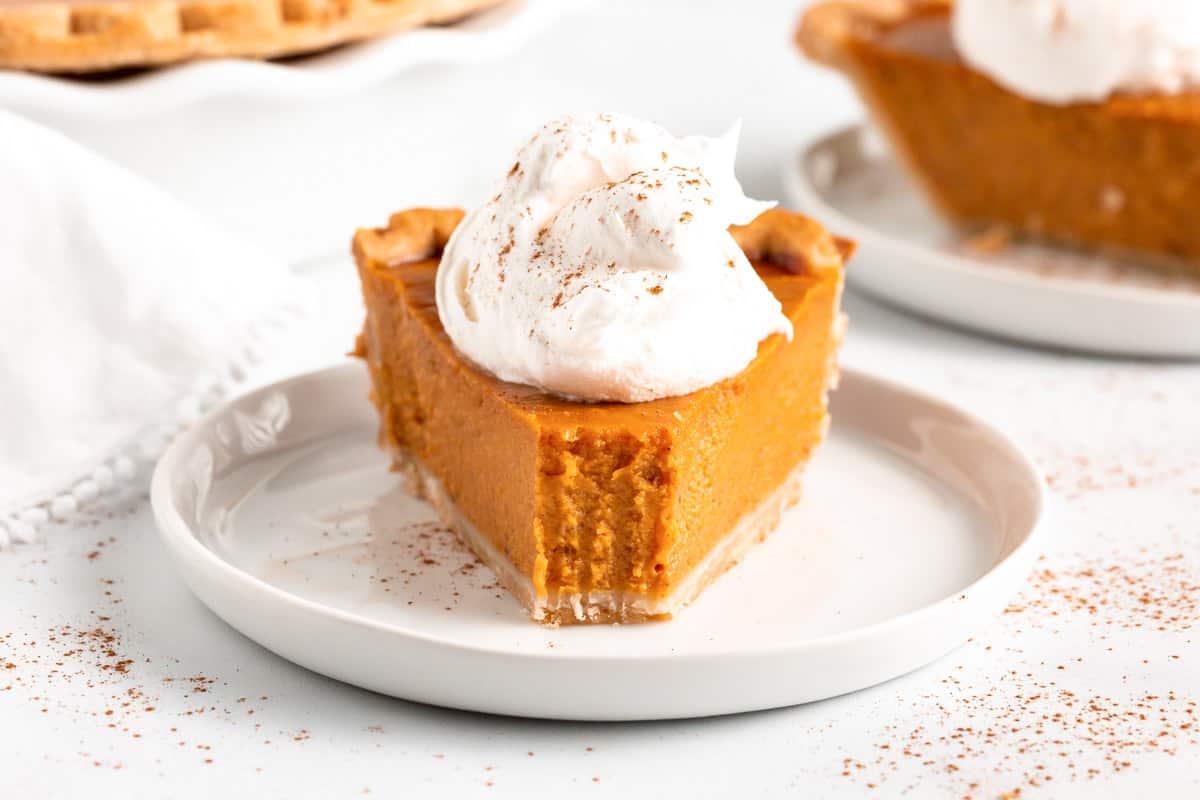 slice of spiced pumpkin pie with velvety smooth filling and whipped cream, cozy autumn setting, warm lighting