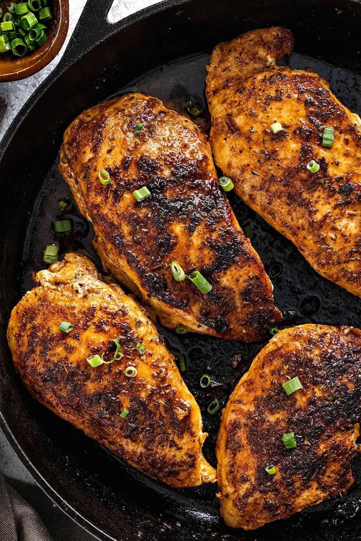 Close-up of chicken searing in a cast iron pan with a vibrant Cajun seasoning blend
