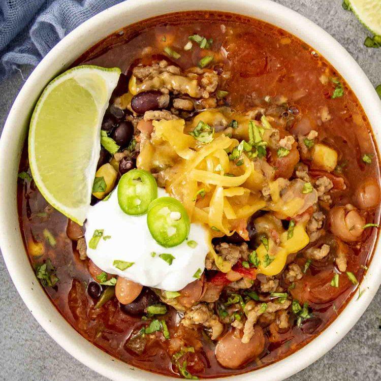 A steaming bowl of smoky taco beef soup garnished with fresh cilantro and a dollop of sour cream on a rustic wooden table.