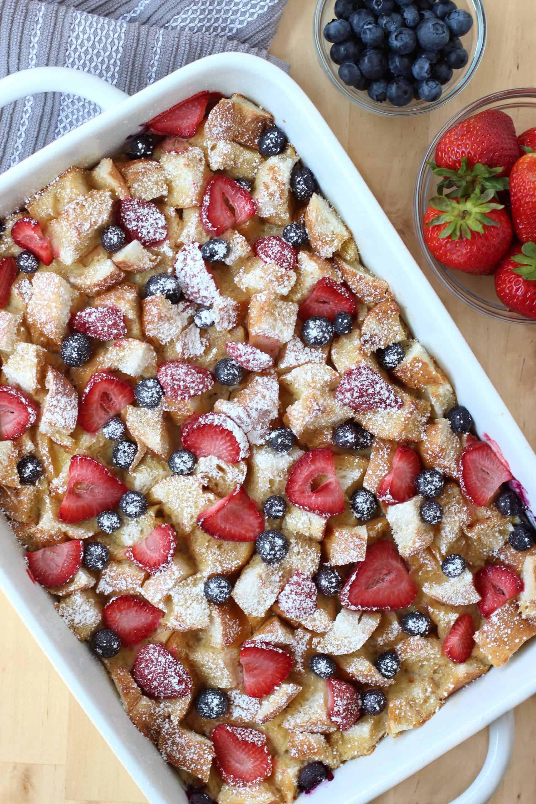 hands adding fresh berries and maple syrup to a french toast casserole