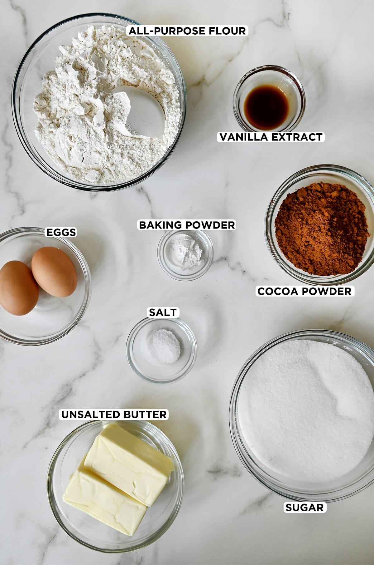 ingredients for cocoa sugar cookies laid out on a marble counter, including Dutch-processed cocoa powder, butter, sugar, and flour