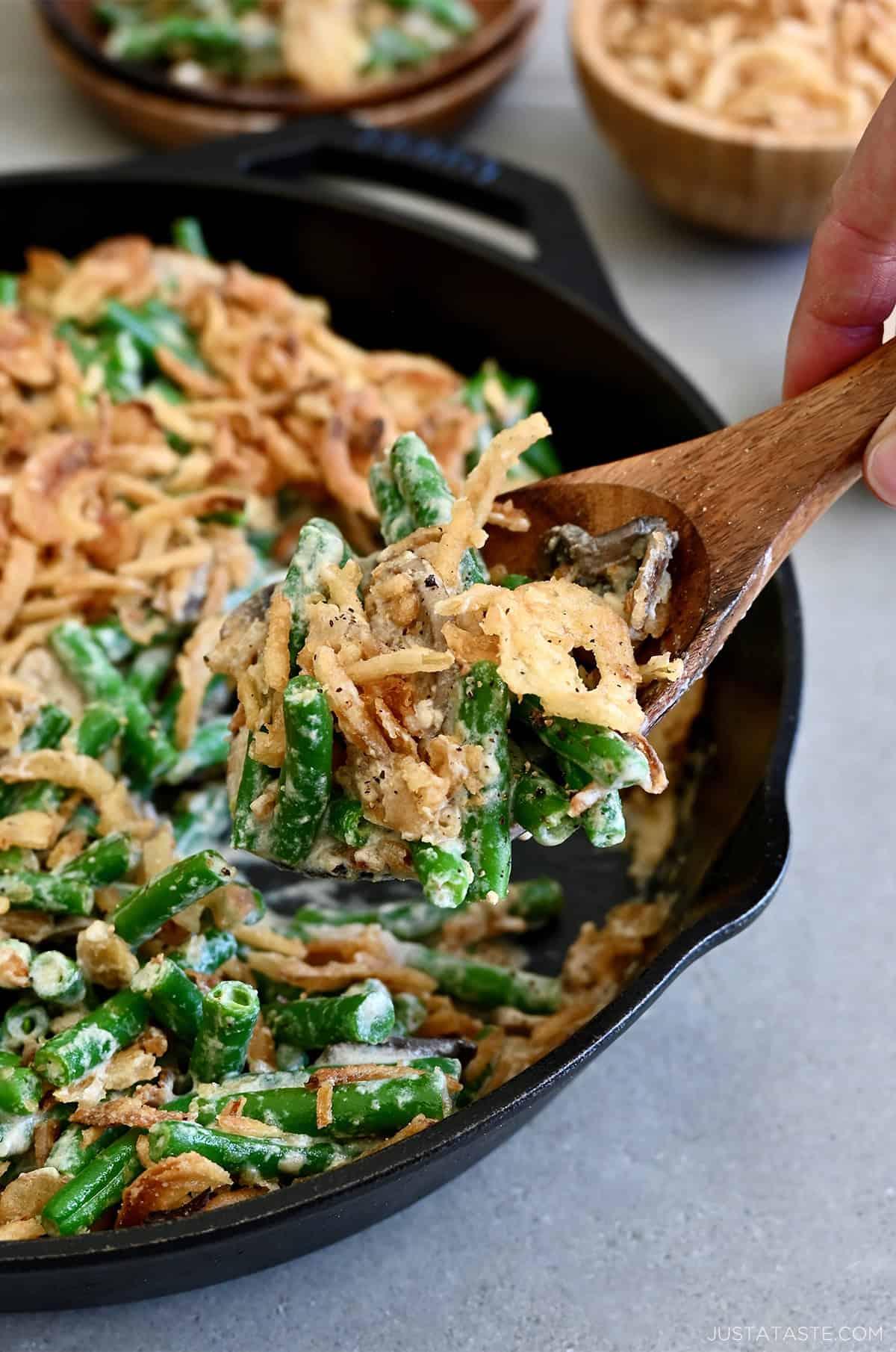 A spatula scooping a generous portion of green bean casserole, showing steam rising and the creamy texture and crispy onions.