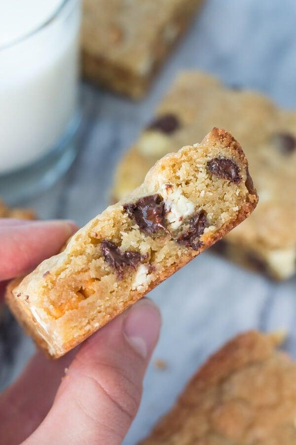 Hand holding a square slice of triple-chip cookie slab, showing its thick, chewy interior and visible chocolate chips