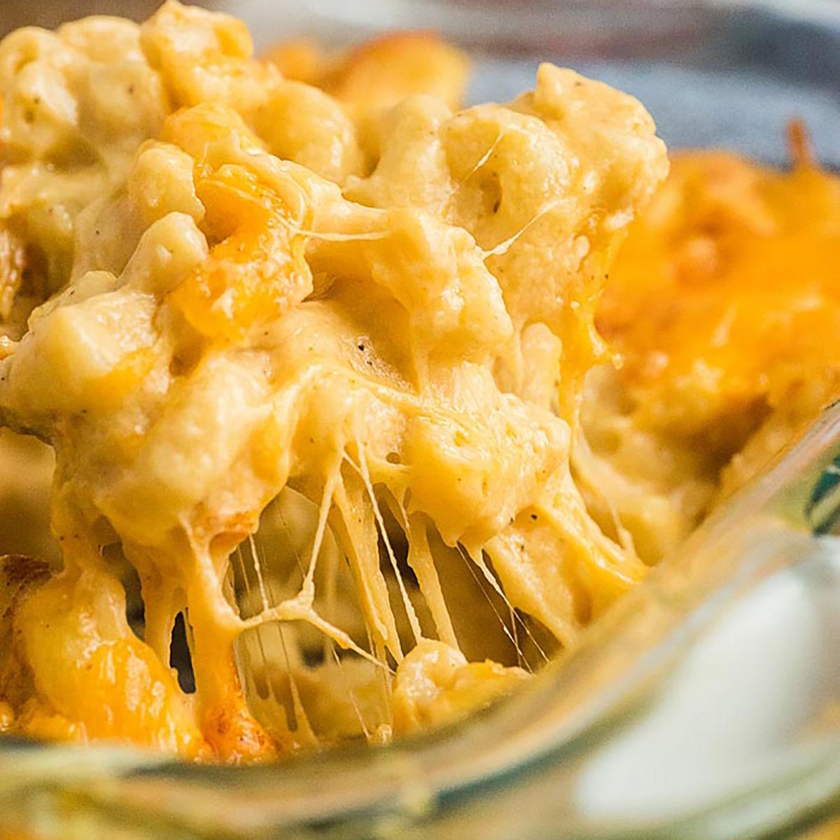 close up shot of gooey, melted cheese sauce being poured over cooked macaroni pasta