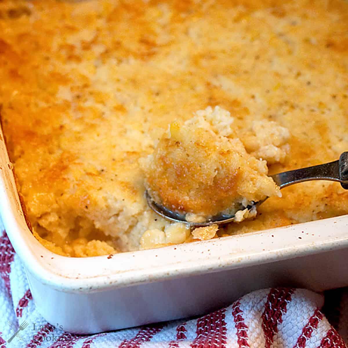 Close-up of golden brown corn casserole with a spoon scooping a soft portion