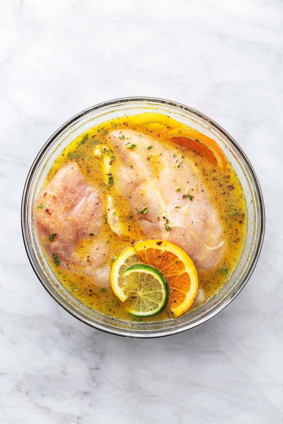 Close-up of raw chicken marinating in a bowl with citrus slices and fresh herbs
