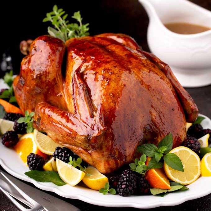beautifully golden brown slow roasted turkey with gravy boat, garnished with herbs