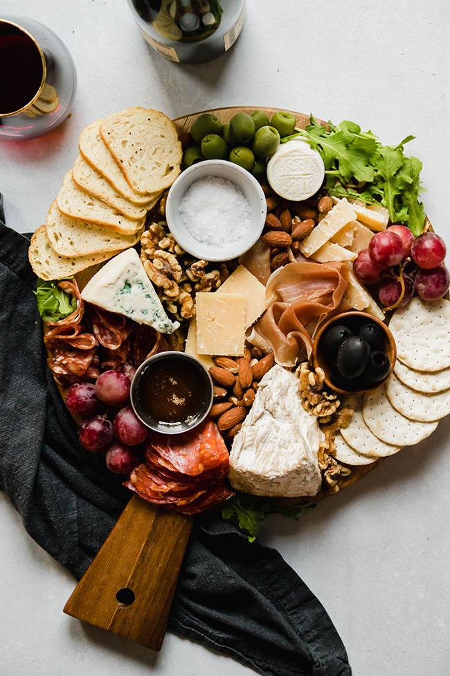 person arranging different types of cheese on a wooden platter