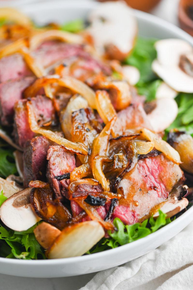 close up of steak salad with dijon mustard dressing being drizzled