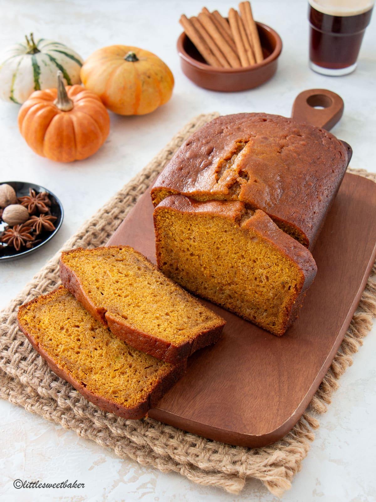 a loaf of moist pumpkin bread sliced on a wooden cutting board