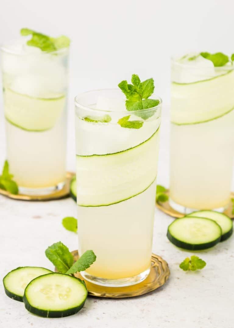 overhead shot of ingredients for cucumber mint cooler, including fresh cucumbers, mint leaves, lime, and honey, laid out on a wooden surface