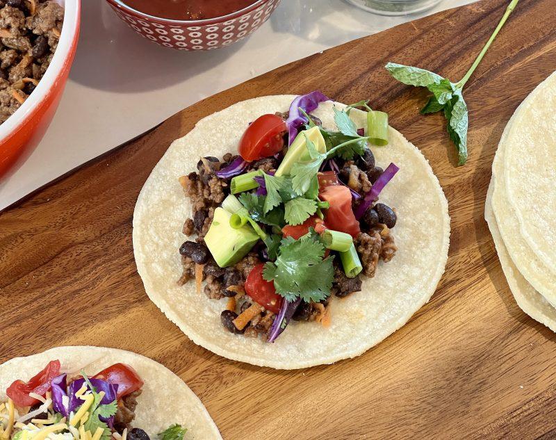 overhead shot of black bean corn ground beef tacos with various toppings scattered around
