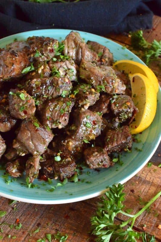 Close-up of chili-roasted beef cubes with fresh herbs on a rustic platter
