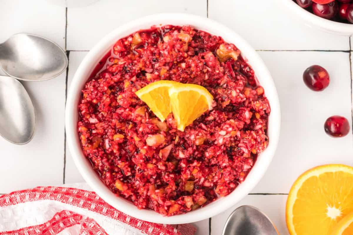 Close-up shot of vibrant orange zest and fresh cranberries being mixed in a bowl, showing the bright colors