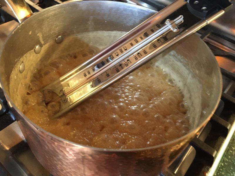 close up of caramel mixture simmering in a heavy saucepan with a candy thermometer