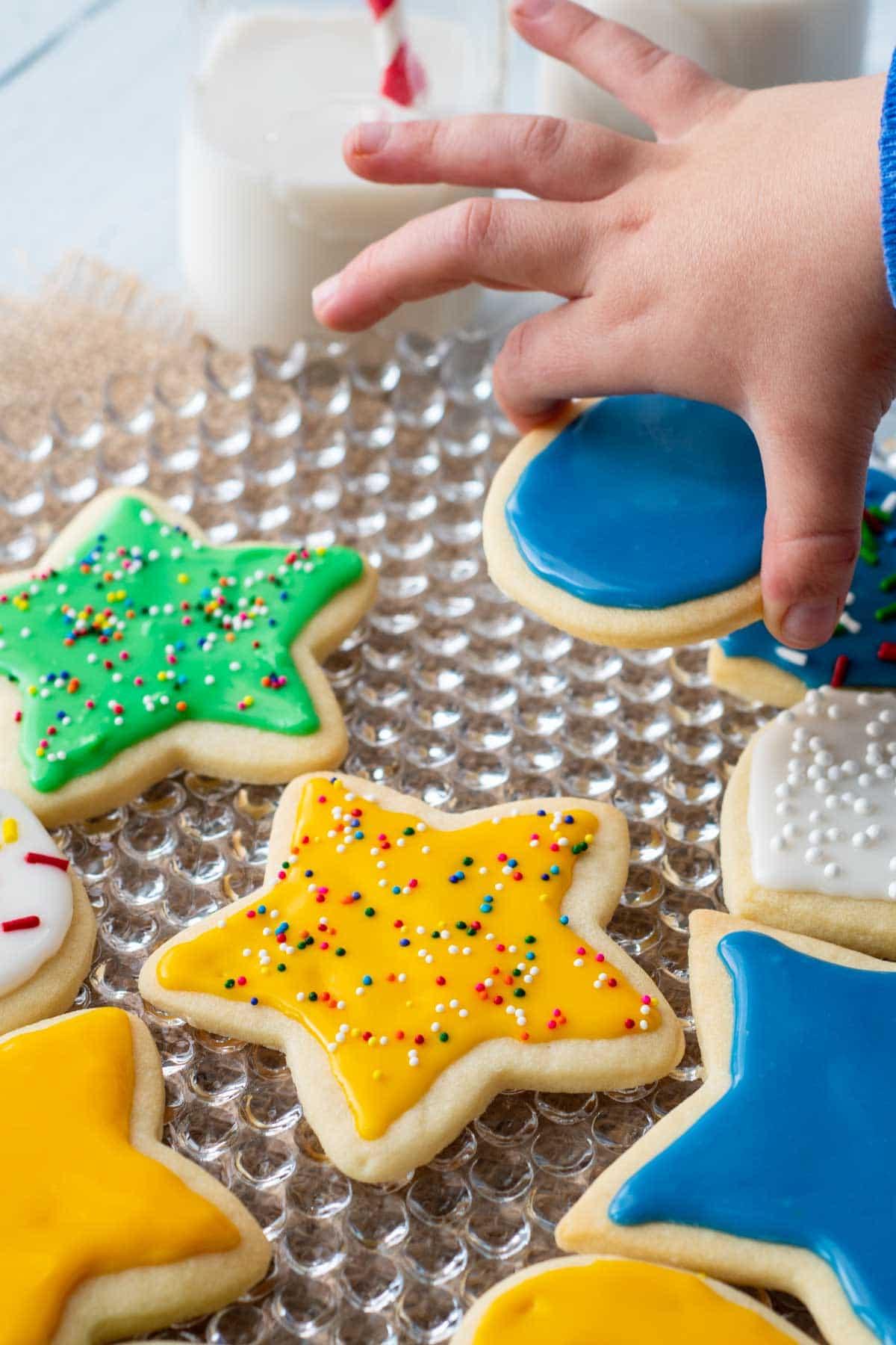 Hands mixing powdered sugar and milk for colorful cookie glaze in small bowls