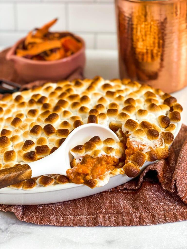 various holiday dishes on a table, with sweet potato casserole prominently featured, warm lighting, hands reaching for food