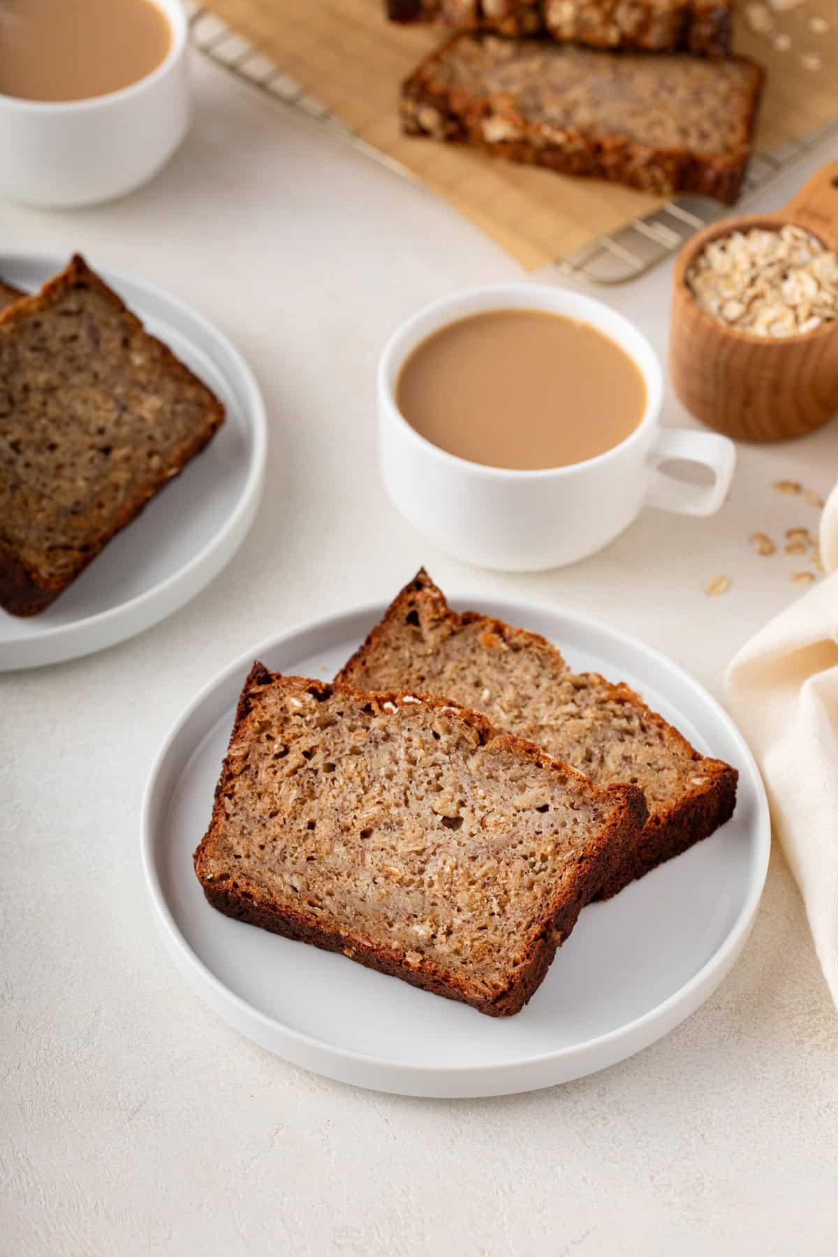 sliced oatmeal banana bread on a white plate with a cup of coffee