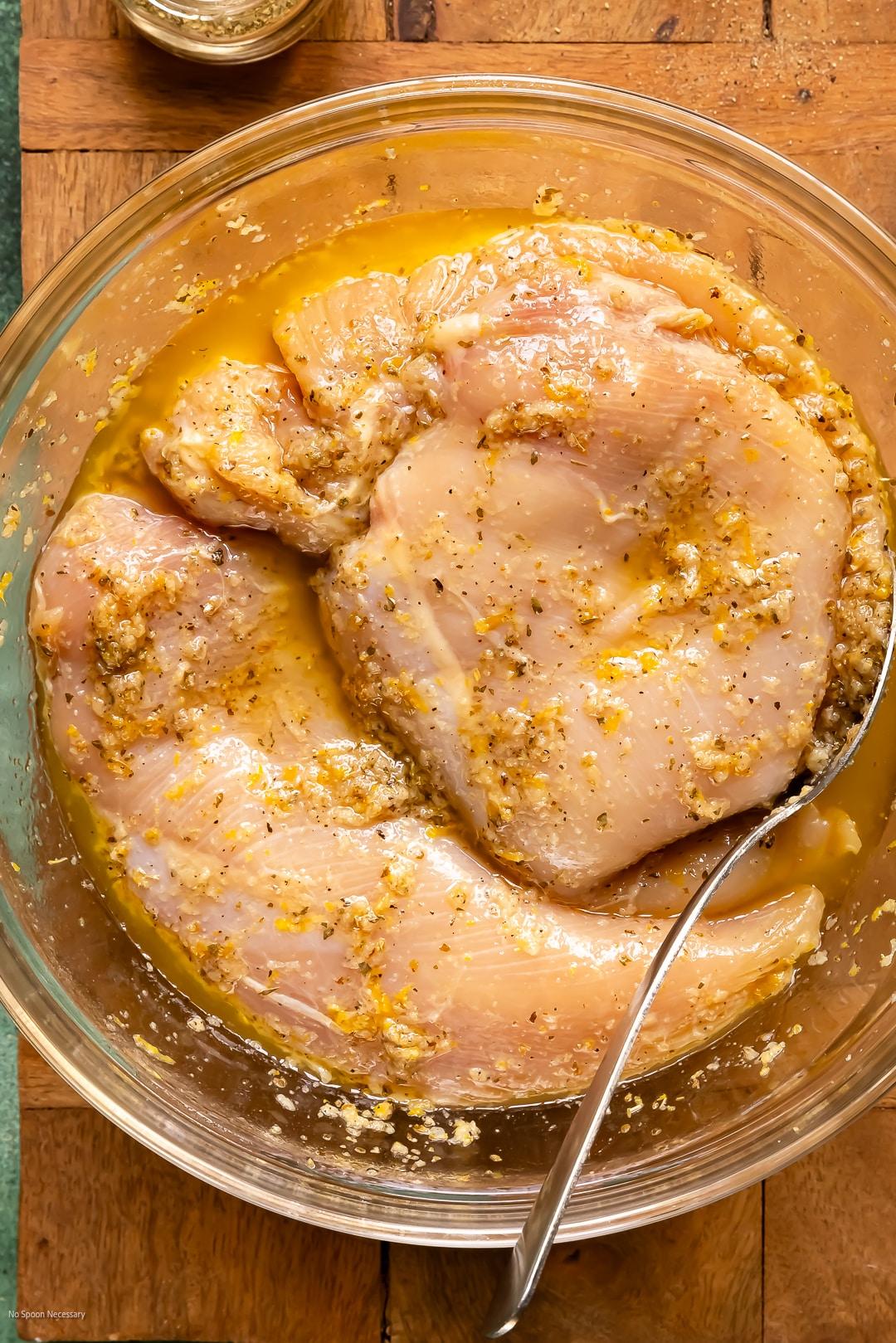 Overhead shot of marinated raw chicken pieces in a bowl with lemon slices and fresh oregano