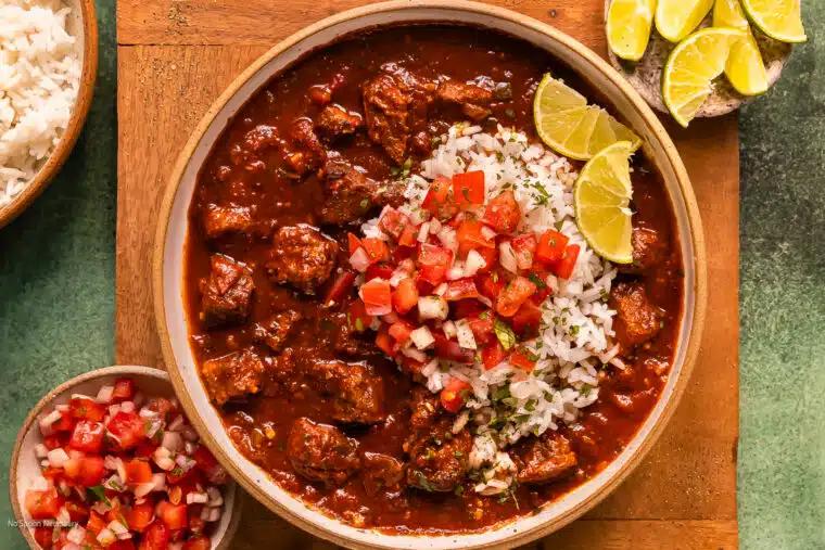 Overhead shot of chili-fired skillet beef served in a bowl with rice, garnished with fresh cilantro, a lime wedge, and a dollop of sour cream.