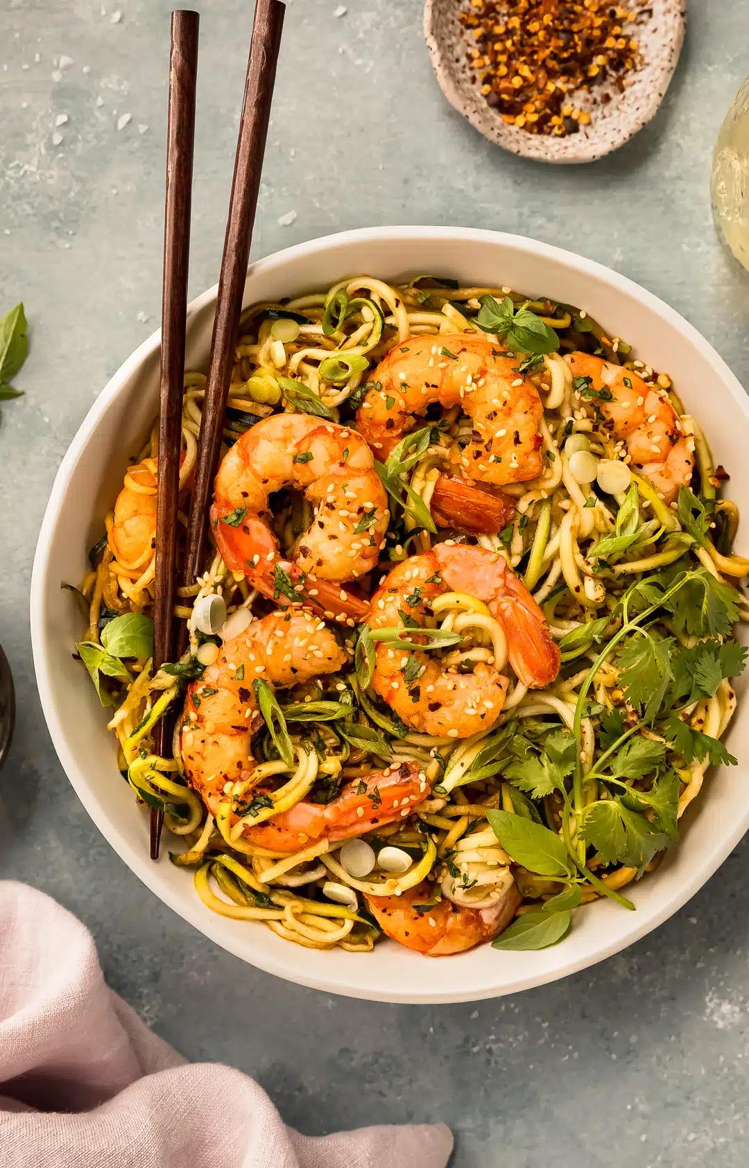 overhead shot of a bowl of lime cilantro zoodle stir fry with blackened shrimp garnished with cilantro and lime wedges