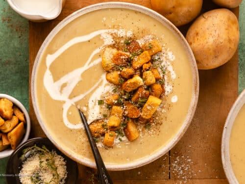 Steaming bowl of creamy roasted garlic potato soup with fresh chives, a slice of crusty bread on the side, cozy lighting, rustic setting