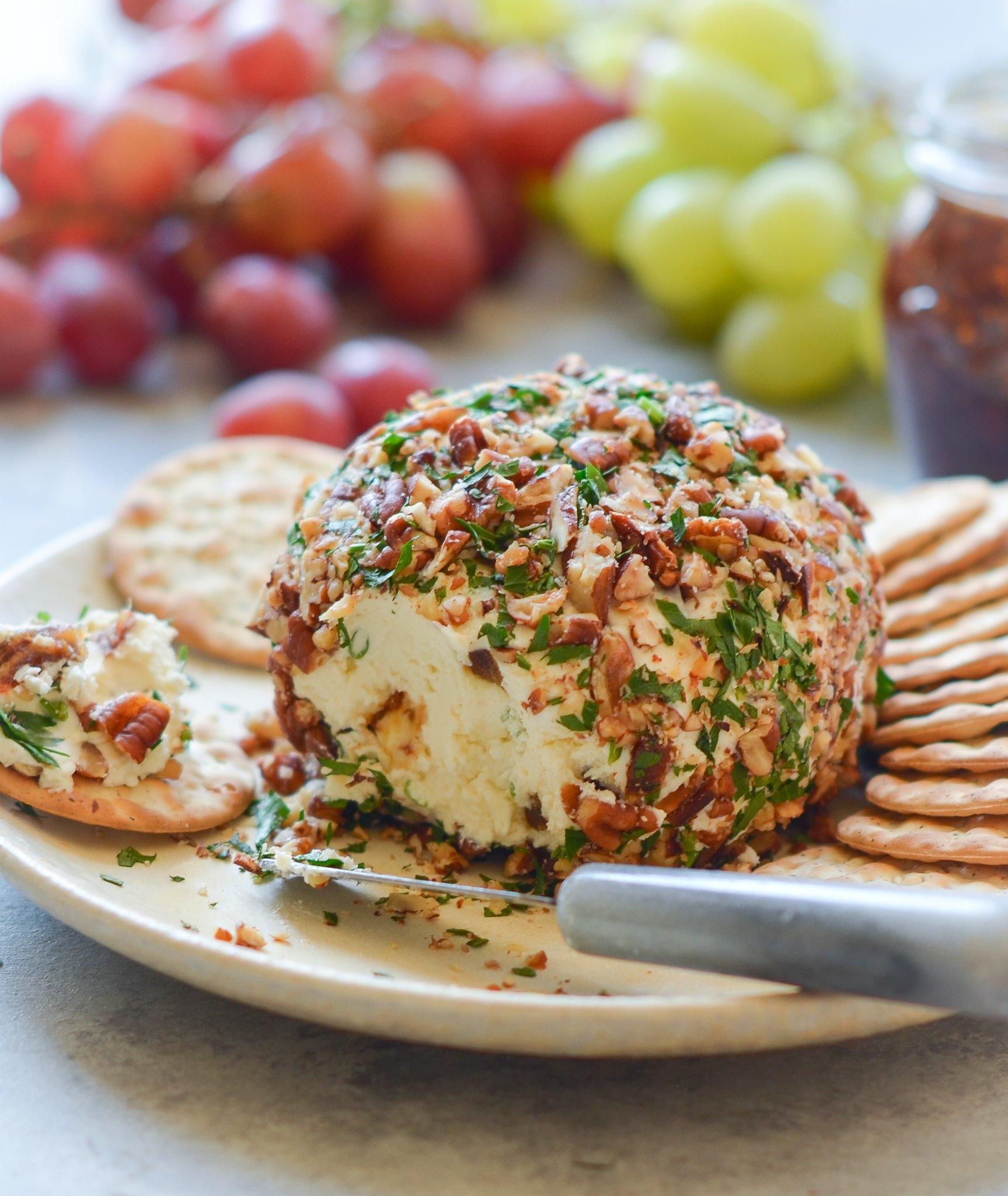 Close-up of a herbed cheese ball being rolled in chopped pecans