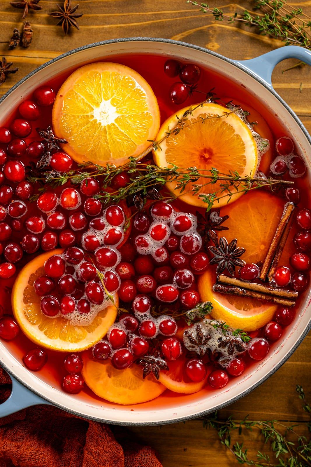 Hands zesting an orange over a pot of simmering cranberries